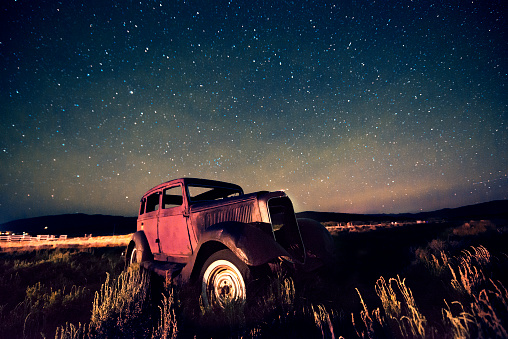 This is a horizontal, color photograph of an abandoned gangster car from the early 1900's abandoned in a field in West Yellowstone, Montana. Shot with a high ISO, shallow depth of field and wide angle lens to capture the starry sky.