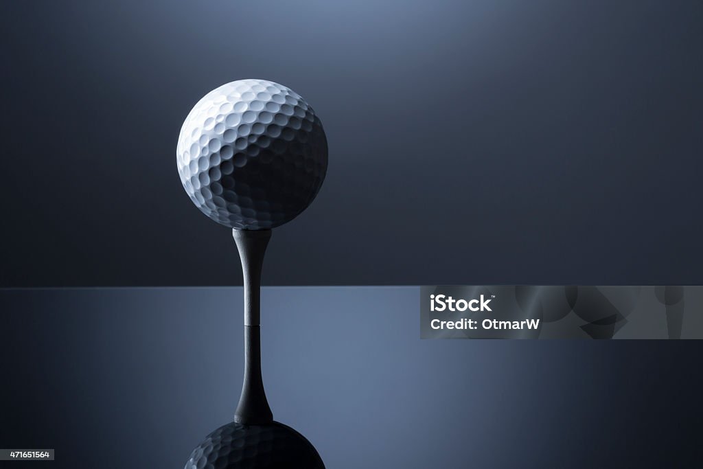 Golf ball over tee isolated on dark blue reflective background. Stylish golf ball on tee isolated on dark blue background with reflection, copy space for text. 2015 Stock Photo