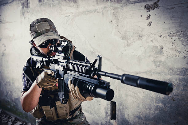 Young Hispanic Modern Army Soldier Aiming with Silenced Assault Rifle stock photo