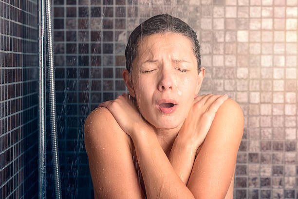 bare woman reacting while taking cold shower - douche stockfoto's en -beelden