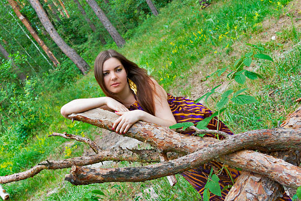 Sad young pretty woman lying on pine logs in the forest