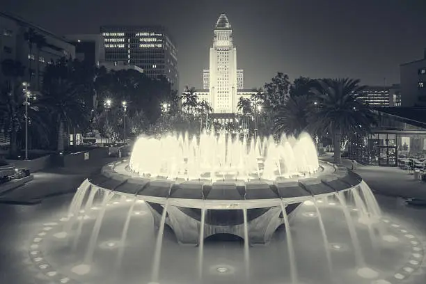 Long exposure black and white photo of Grand Park with fountain and with the city hall of Los Angeles, California in the background at night.