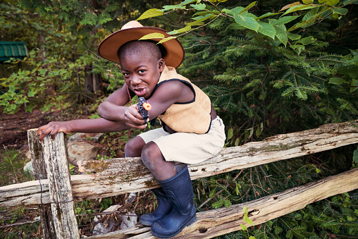 Little black boy playing cowboy pretending that the fence is his horse, aiming with a toy gun. Copy space.