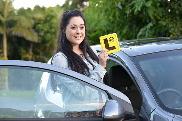 istock Young female driver by an open car holds up yellow L-plate 471665536