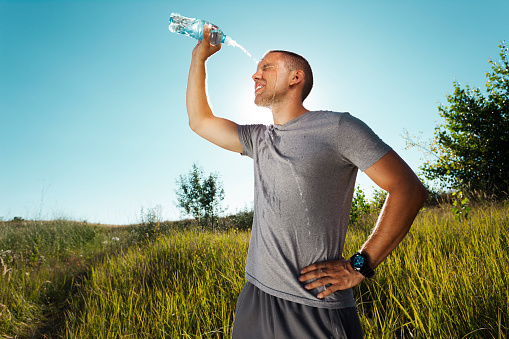 Young man is refreshing himself with water from the bottle after workout in nature.  Grain added to create atmosphere