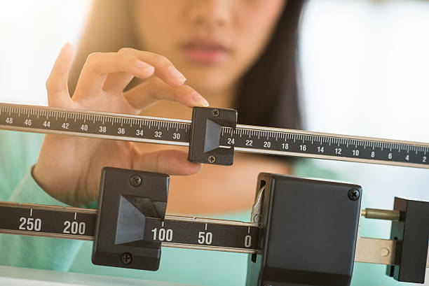 Midsection Of Woman Adjusting Weight Scale Midsection of mid adult Asian woman adjusting balance weight scale diets stock pictures, royalty-free photos & images