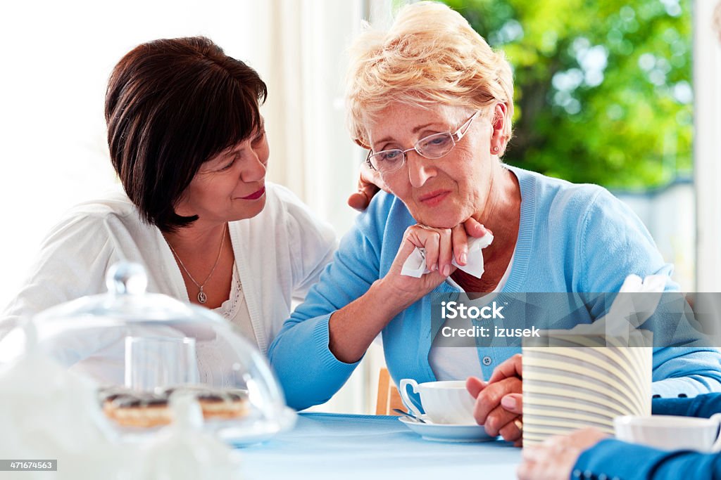 Mature woman consoling her friend Mature woman sitting at the table at home and comforting her unhappy friend. Friendship Stock Photo