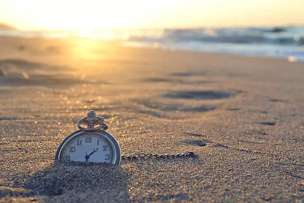 Photo of Pocket watch nestled in the sand of a beach at sunset