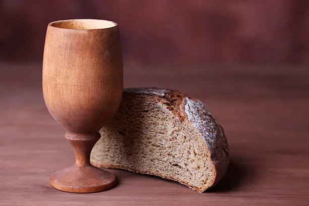 Wooden chalice of wine and bread on the dark background.