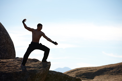 A male athlete kickboxing on the edge of a cliff on a mountain