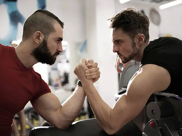 Profile of two serious young men arm wrestling in a health club.