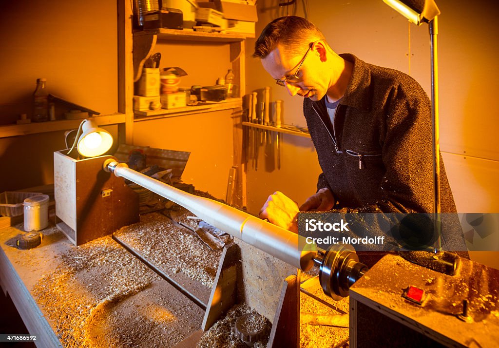 Joiner Working On Lathe Attractive mid adult man working in carpentry workshop. The woodworker is making the wooden baseball bat on the lathe 2015 Stock Photo