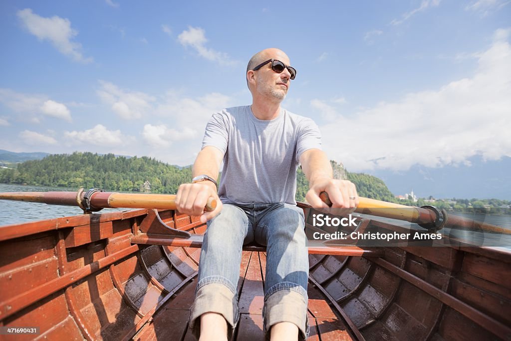 Uomo maturo Remare barca in legno sul lago di - Foto stock royalty-free di 50-54 anni