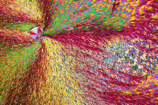 Abstract polarizing micrograph of ascorbic acid crystals, with spiral bands of color. Taken at 100x in a polarizing microscope.