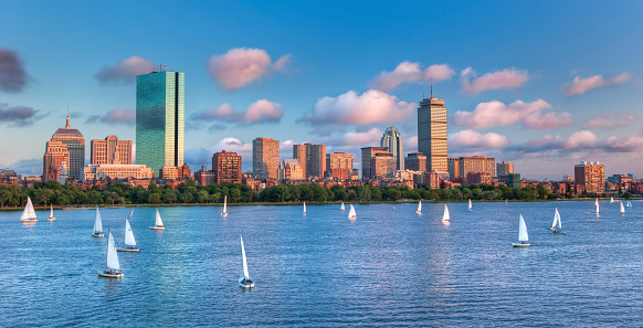 A panoramic view of the full Boston skyline with the Charles River full of sailboats as sunset approaches