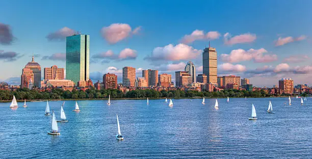 A panoramic view of the full Boston skyline with the Charles River full of sailboats as sunset approaches