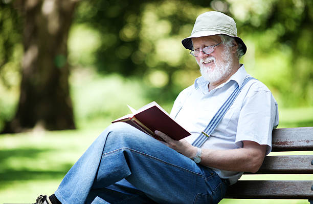 istock Elderly man with beard and hat reading in a park 471699696