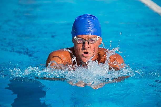 Front view of senior man at breast stroke, selective focus, interesting water splashing