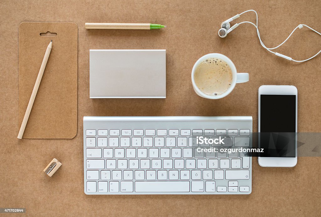 Working desk with keyboard, coffee, cell phone and headphones High angle view of a working desk with computer keyboard, external hard drive, smart phone, coffee, pens and headphones on it. Horizontal composition, High angle view. Image taken with Nikon D800 and developed from Raw 2015 Stock Photo