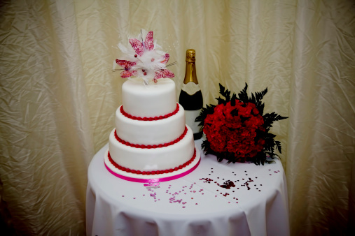 White frosting wedding cake decorated with pink ribbons and flowers for an evening nuptial ceremony