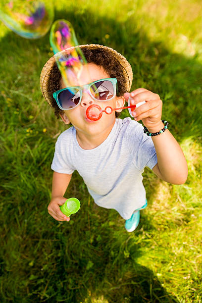 pequeño niño divirtiéndose soplando burbujas - bubble child bubble wand blowing fotografías e imágenes de stock