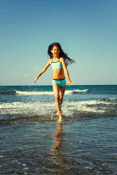 istock Young girl having fun running through the splashing waves 471715932