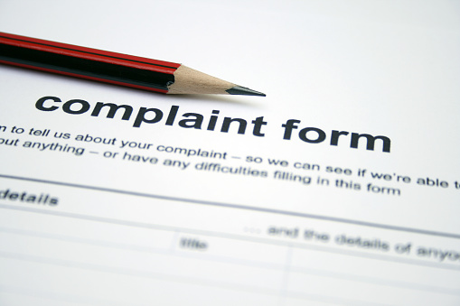 A red sharpened pencil sits on the heading of a blank complaint form.  The form has black text printed on white paper.