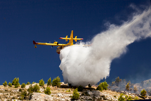 A twin-engined water bomber dumping its load on a fire in the mountains
