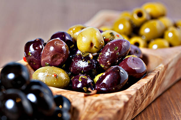 Variety of green, black and mixed marinated olives Variety of green, black and mixed marinated olives in olive tree dish on wooden table. Selective focus marinade stock pictures, royalty-free photos & images