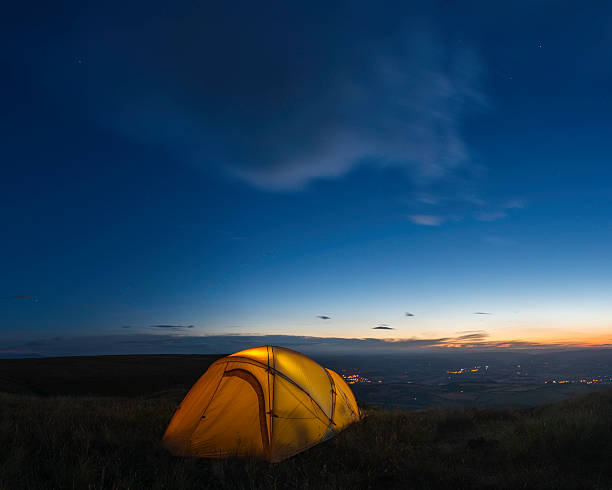 istock Stars shining over glowing yellow tent on mountain overlooking valley 471729045