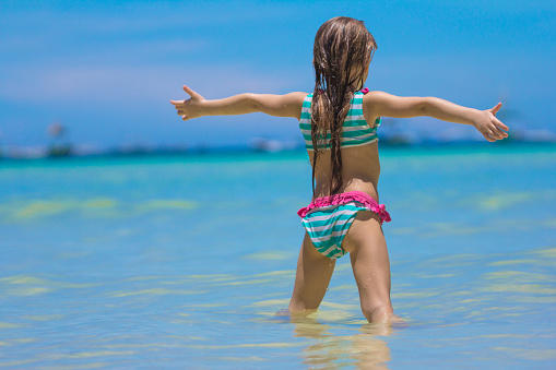 Beautiful little girl spread her arms standing at the beach