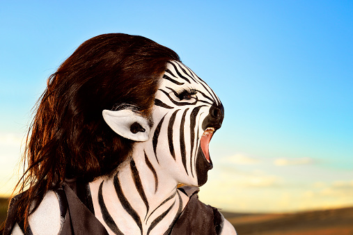 From out of Africa . . . A braying humanoid - part Zebra.  Her mouth is open wide as she brays her story to the world .  Blue skies behind and to the right leave plenty of copy space.  Dunes in the lower right hand corner give contrast and intrest.  Stripes on the zebra with long, pointed ears and huge lone eyelashes.