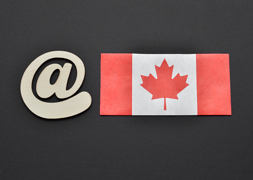 Close up of the at sign next to a Canada Flag on a black background.  