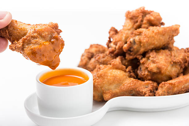 Human hand holding a buffalo chicken wing dipped in hot sauce on white background