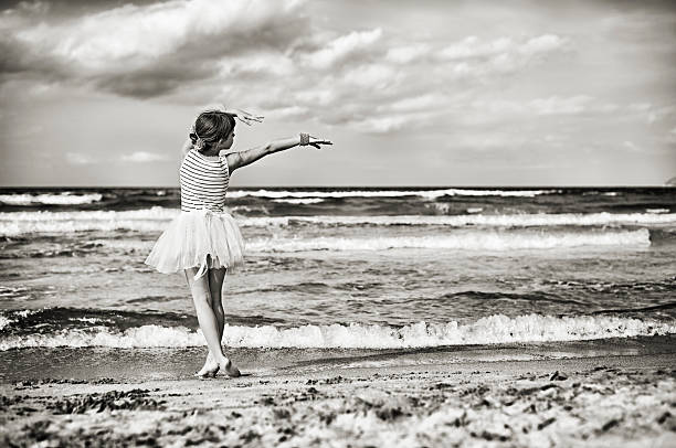 Little girl dancing ballet on the beach. Monochrome with a drop of sepia. Fine noise applied.