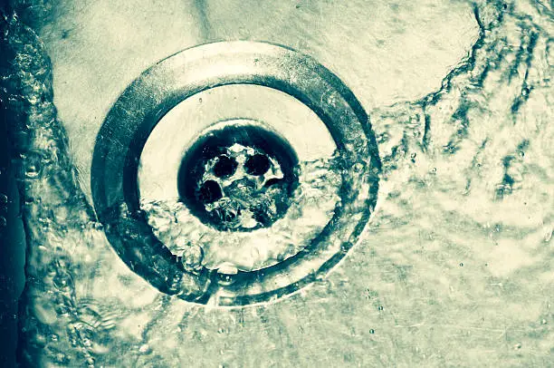 Water running down plughole in stainless steel sink.