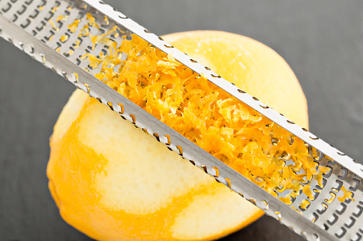 A high angle close up shot of a chef zesting a lemon with a microplane grater.
