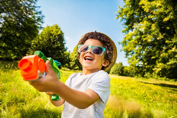 Photo of Laughing kid playing with squirt gun in park