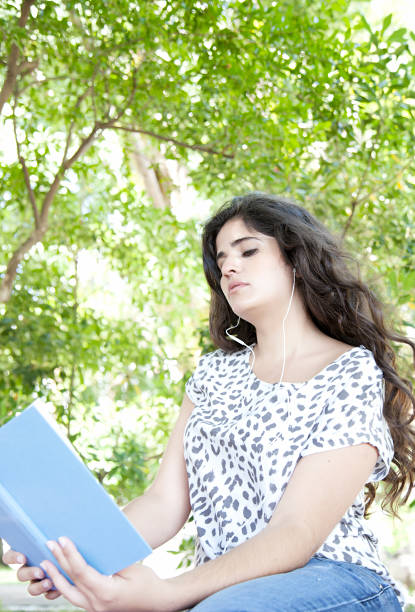 istock Young woman reading a book at the park 471756419