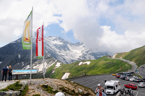 Grossglockner, Austria - July 21, 2013: Parking place on a viewing platform on the Grossglockner High Alpine Road (Salzburg, Austria). Cars and mobile home parked. People wander around and enjoy the view. A couple on a information table about mountain names.
