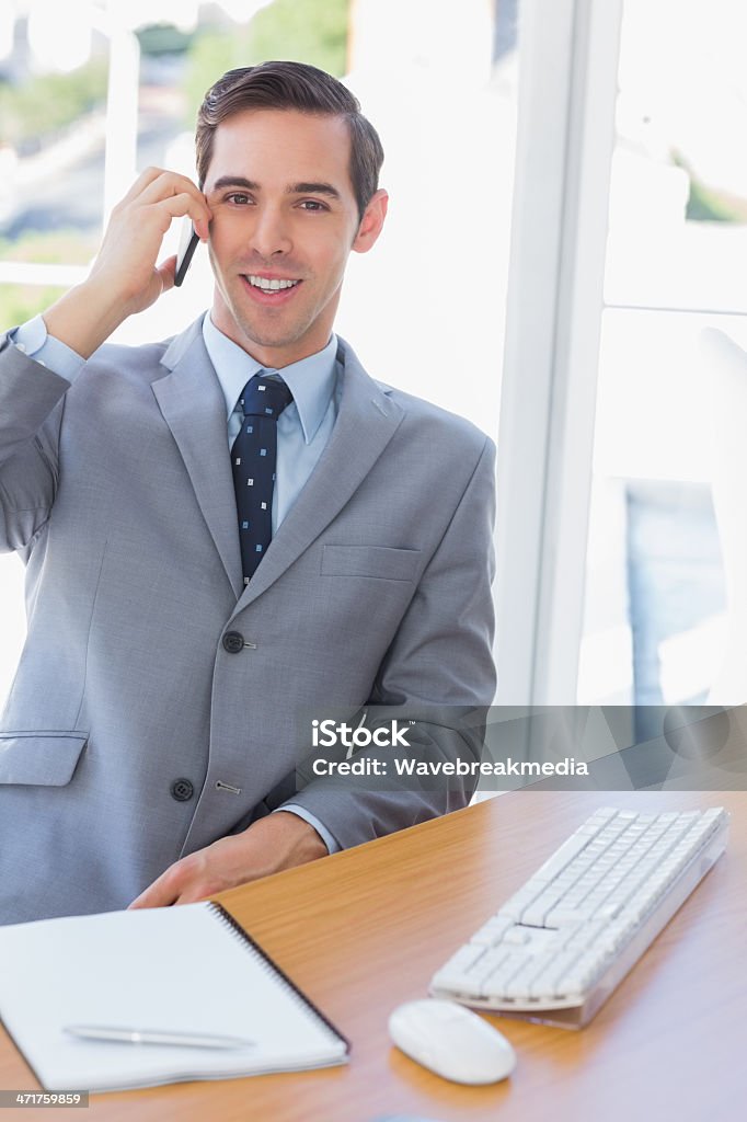 Uśmiechająca się Biznesmen na telefon, patrząc na kamery - Zbiór zdjęć royalty-free (Biurko)