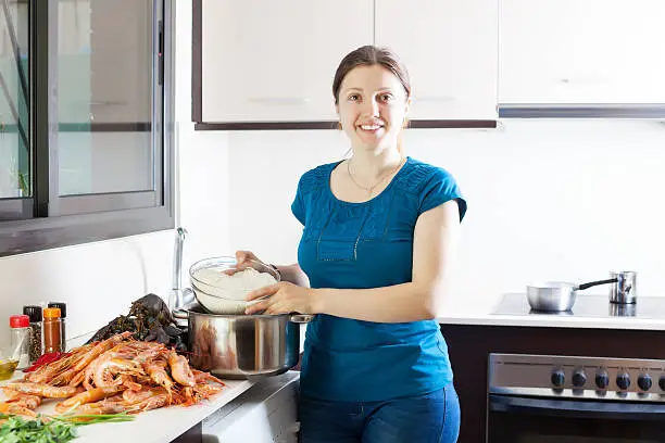 Happy woman cooking rice with seafoods in kitchen
