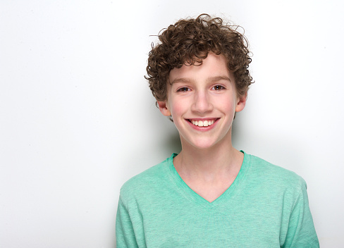 Close up portrait of a happy young boy with curly hair smiling against white background