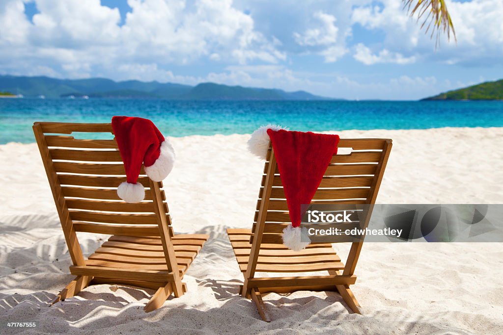 Cadeiras com chapéus de Natal sob as palmeiras em uma praia - Foto de stock de Cadeira de Praia royalty-free