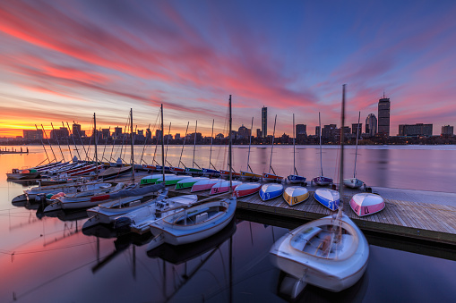 Boston skyline at sunrise as seen across the Charles River from Cambridge, with sailboats moored on the river