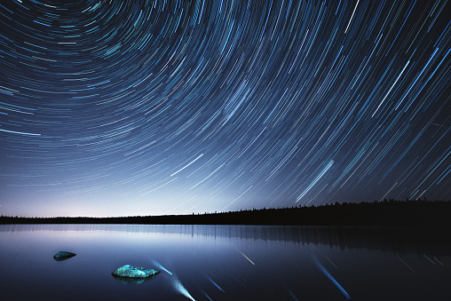 A 50 minute lapse in time showing Earth's rotation over a still lake.  Light pollution on the horizon from a nearby city.  Long exposure shot at high iso.