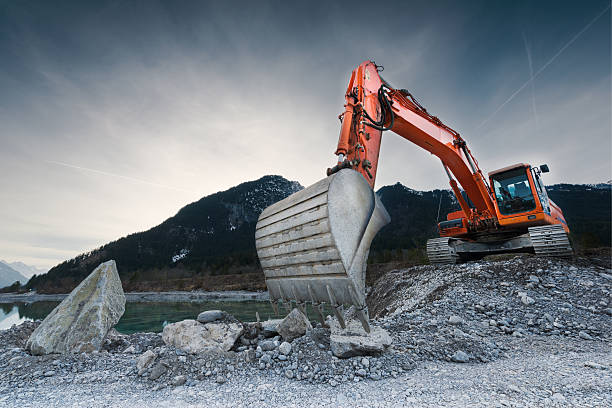heavy organge excavator with shovel standing on hill with rocks heavy organge excavator with shovel standing on hill with rocks earthwork stock pictures, royalty-free photos & images