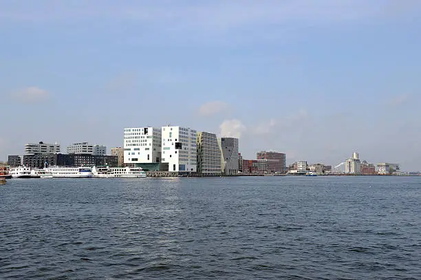 A view at the modern office buildings and appartements on the south bank of the river IJ in Amsterdam. This area on the West side of the Central Railway Station is locally called "IJdok" and "Westerdok". The large white building is the new Palace of Justice and the river cruise ships dock on the left side.