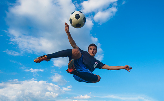 Young male soccer player performing side volley kick in mid-air against the blue sky