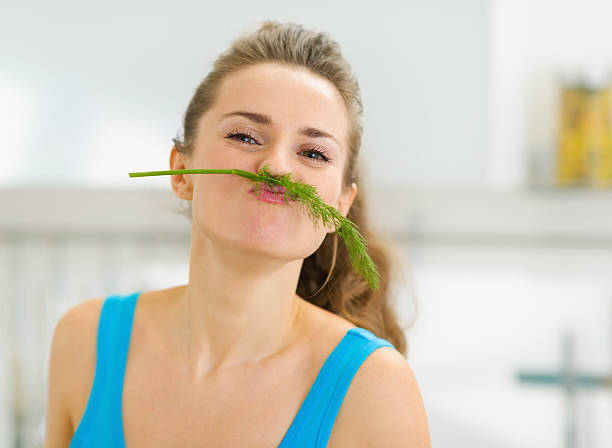 istock Funny young woman using dill as mustache in kitchen 471785713